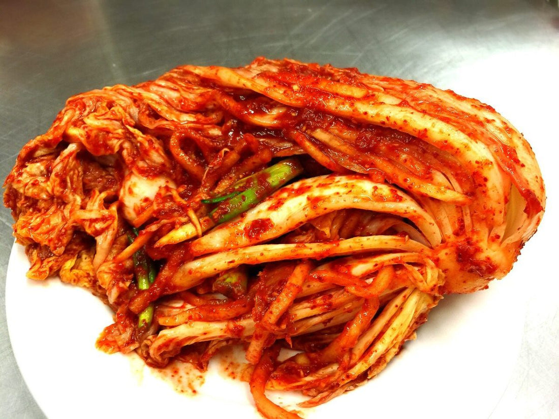 A whole napa cabbage kimchi coated in red chilli seasoning, with spring onion, on a white plate
