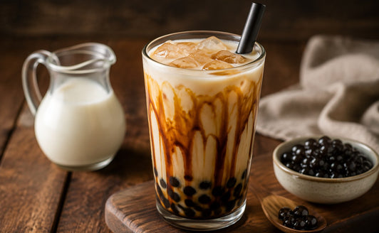 Brown sugar bubble tea with tapioca pearls in a tall glass beside a milk jug