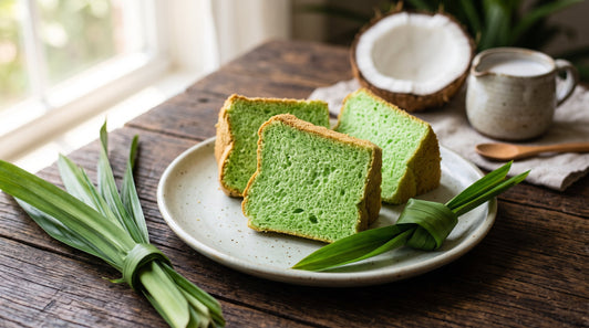 Slices of bright green pandan chiffon cake on a plate with fresh pandan leaves and coconut
