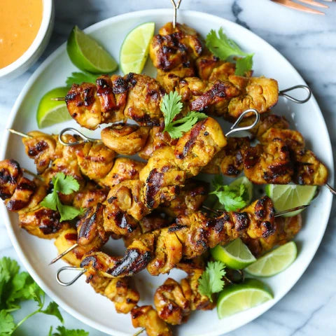 Delicious 🍗 peanut chicken satay skewers recipe served with 🍋 lime wedges and fresh cilantro on a white plate.