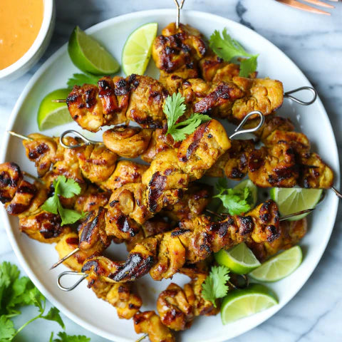 Delicious 🍗 peanut chicken satay skewers recipe served with 🍋 lime wedges and fresh cilantro on a white plate.